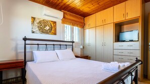 A bedroom with a bed, wooden wardrobe, TV, and artwork. - Seaview Nature Retreat - Filiatra s Cozy Hideaway (Trifylia)
