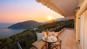 A balcony with a table set for two, overlooking a scenic view of the sea and mountains during sunset. - Ionian View Haven - Parga Paradise (Parga)