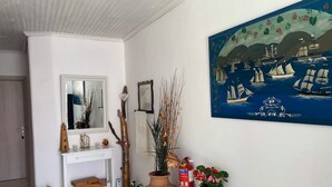 A room with a white console table, a mirror, a painting of sailing ships, and a large potted plant.