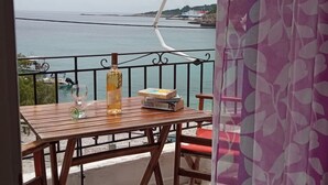 A balcony with a table, a bottle, and books. The view includes a body of water and a distant shoreline.