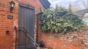 A brick building with a dark wooden door, a small potted plant, and a metal staircase leading to the entrance.