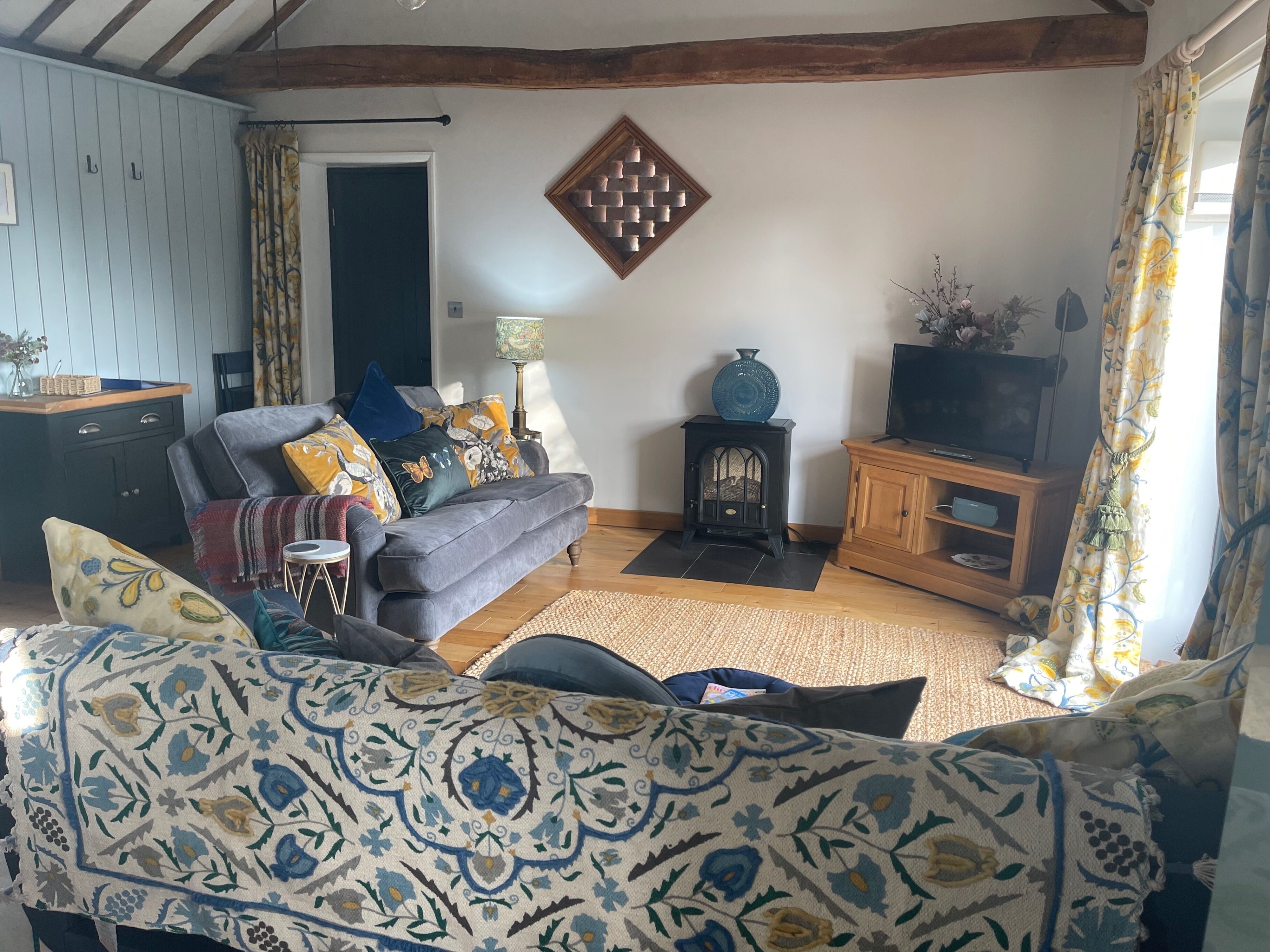 A cozy living room with a sofa, a small wooden TV stand, a decorative wall piece, and a patterned rug.