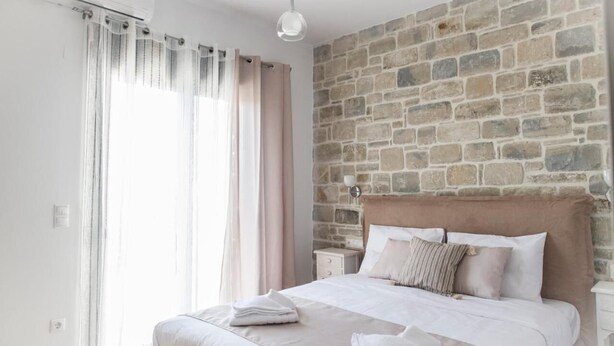 A bedroom with a stone wall, a bed with white linens, a nightstand, and a hanging light fixture. - Villa Mira (Kamilari)