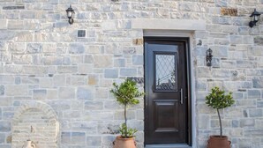 A stone building with a dark door, two potted plants, and a small table with a vase. - Villa Mira (Kamilari)
