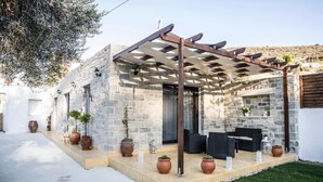 A stone building with a pergola, outdoor seating, and potted plants. - Villa Mira (Kamilari)