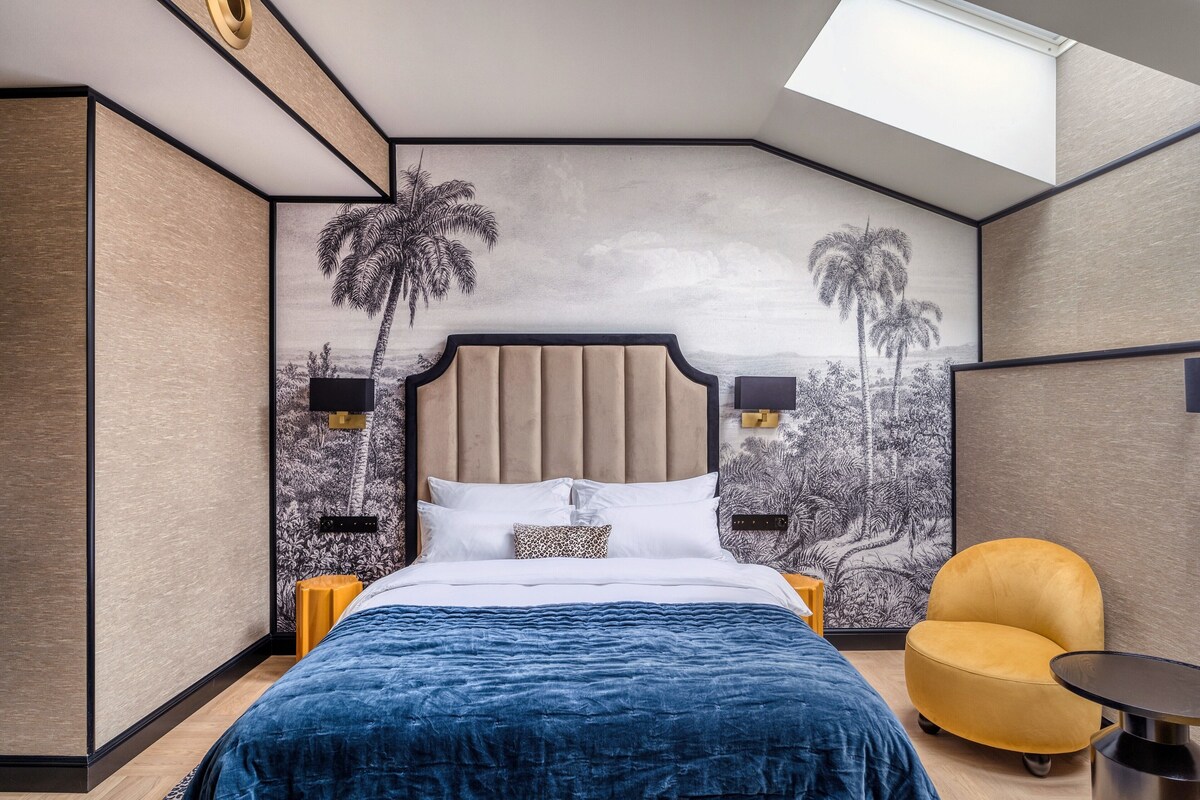 Un dormitorio con una cama grande, dos lámparas de pared, un sillón amarillo y un tragaluz.
