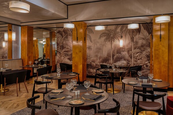 Un restaurante con mesas redondas, sillas y un mural tropical en la pared.