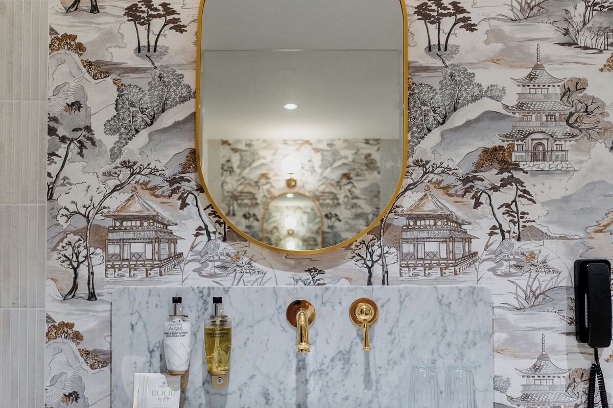 Une salle de bain avec un lavabo en marbre, des robinetteries dorées et un papier peint de style asiatique traditionnel.