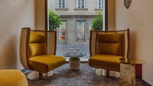 Un interior moderno con dos sillones, una mesa de vidrio, piso con diseño y vista a una calle con edificios y áreas verdes.
