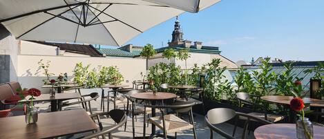 An outdoor seating area with tables and chairs, umbrellas, and potted plants.
