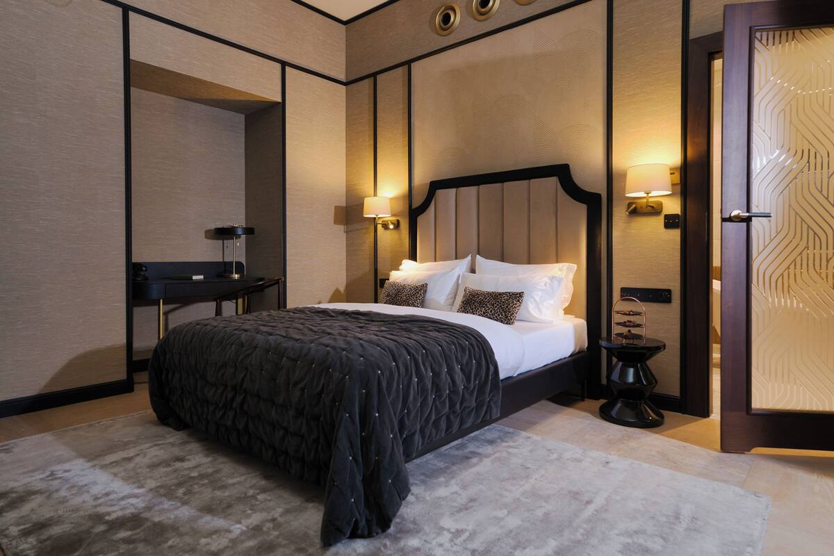 A modern hotel room with a large bed, a bedside table, a nightstand, and a mirror.