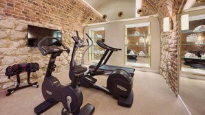 Un gimnasio con paredes de ladrillo, equipo de ejercicio, un televisor y vitrinas de vidrio.
