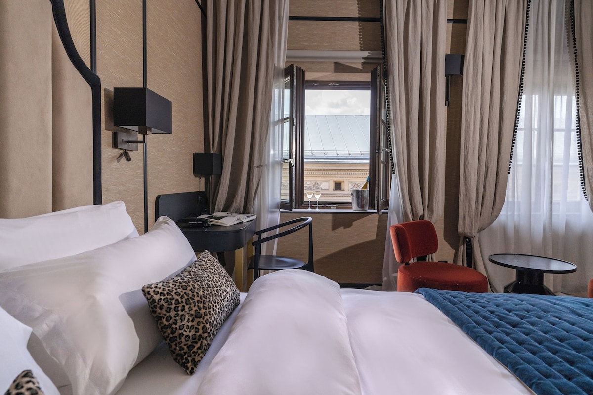 Habitación de hotel con cama, escritorio, silla, una mesita y vistas al exterior.