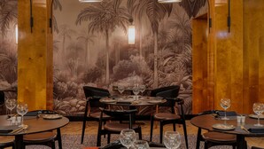 Un restaurante con mesas redondas, sillas negras y un mural tropical en la pared.