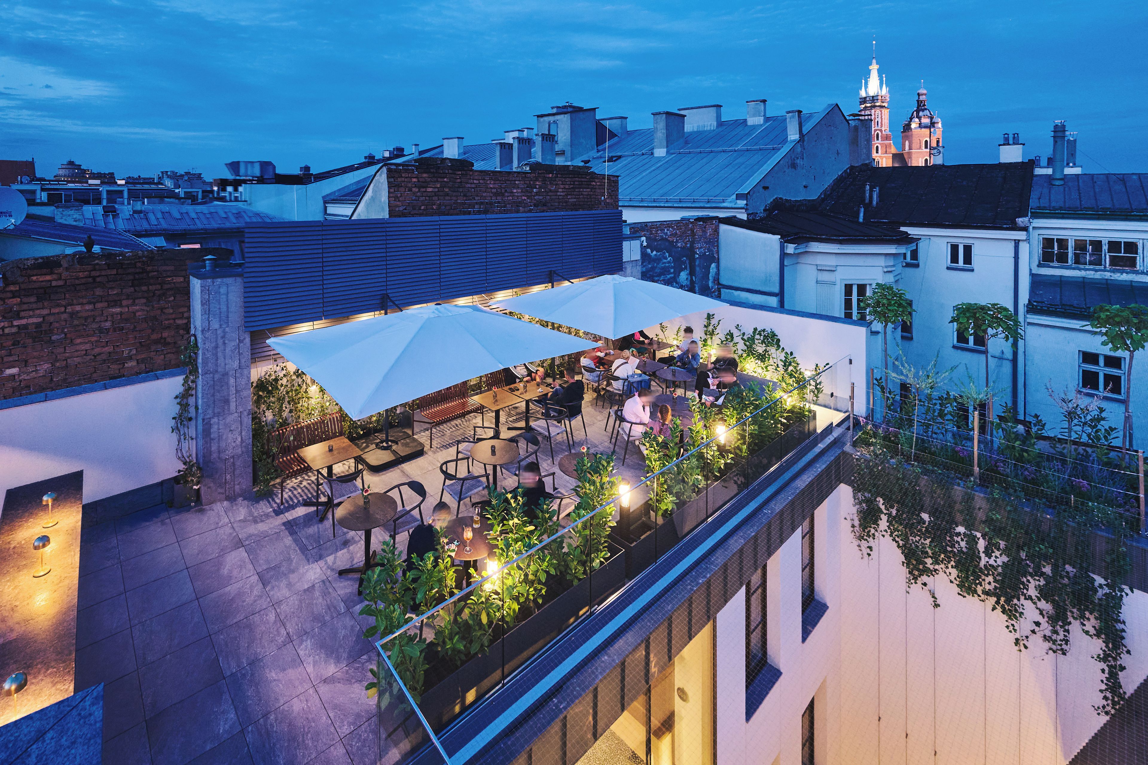 En udendørs terrasse med borde og stole, omgivet af en lav mur og beplantning.