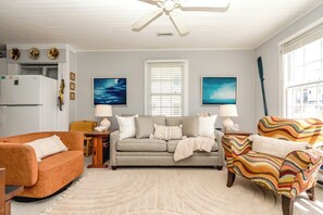 A living room with a sofa, two armchairs, a ceiling fan, and artwork on the walls.
