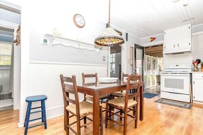 A dining area with a wooden table and chairs, a hanging light fixture, and a kitchen with white cabinets. - Sunshine Trio - Cute 2BR Cottage! Dog Friendly & Easy Beach Access (Surf City)