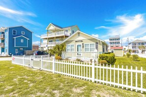 A residential area with a two-story house featuring a balcony, a white picket fence, and a well-maintained lawn.