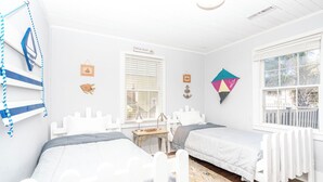 Una habitación con dos camas, una ventana con persianas, una mesita pequeña y adornos en la pared, incluyendo una cabeza de pez y una fotografía enmarcada.