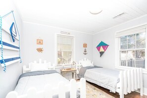 A room with two beds, a window with blinds, a small table, and wall decorations including a fish head and a framed picture. - Sunshine Trio - Cute 2BR Cottage! Dog Friendly & Easy Beach Access (Surf City)