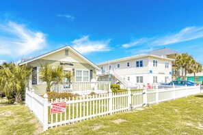 A vacation rental property with a white picket fence, a covered porch, and a two-story building. - Sunshine Trio - Cute 2BR Cottage! Dog Friendly & Easy Beach Access (Surf City)