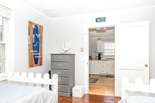 A room with a bed, a dresser, a mirror, and a door leading to a kitchen.