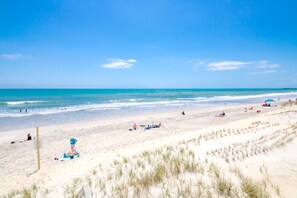 A beach with people sunbathing and swimming, a wooden fence, and dunes in the foreground. - Sunshine Trio - Cute 2BR Cottage! Dog Friendly & Easy Beach Access (Surf City)