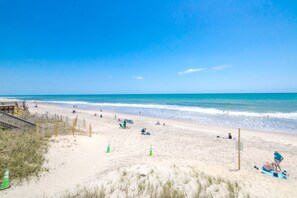 A beach with a wooden boardwalk, beachgoers, and a clear blue sky.