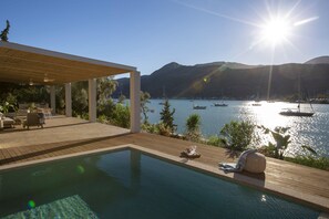 Un espace piscine doté d’une terrasse en bois, de chaises longues et offrant une vue sur les bateaux sur un lac.