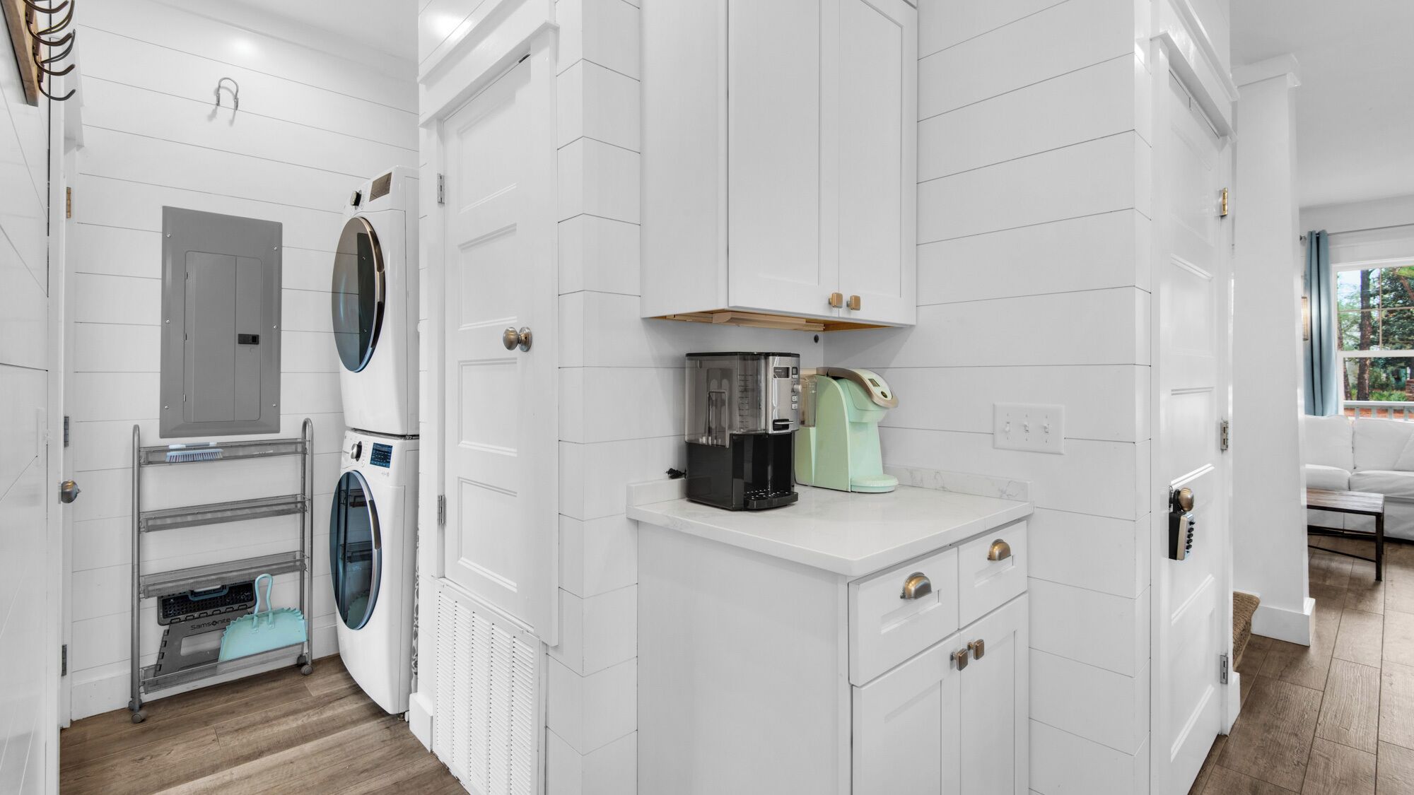Une buanderie équipée de machines à laver et de sèche-linge superposés, d’une machine à café et d’un petit meuble de rangement.