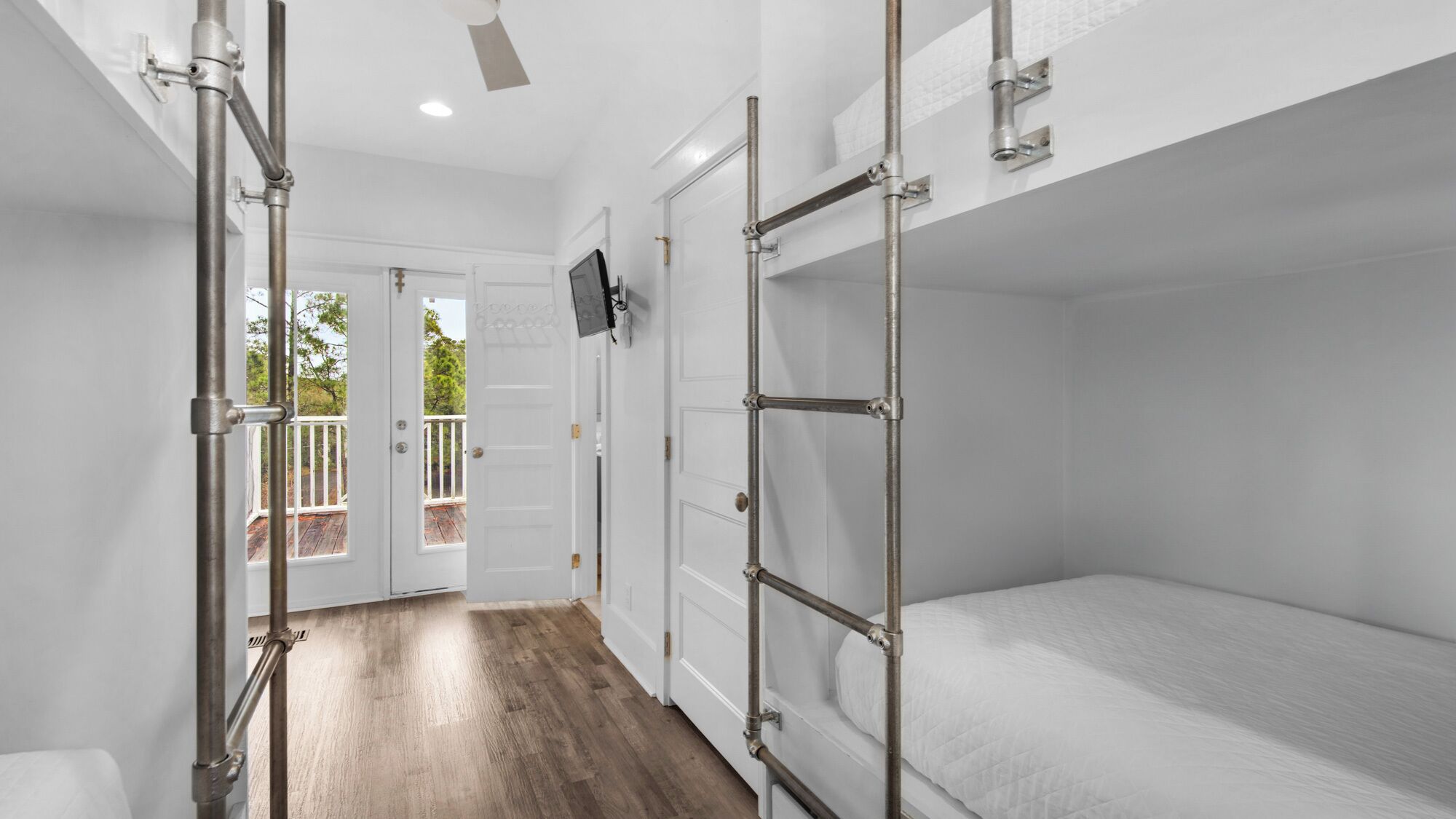 A room with bunk beds, a TV mounted on the wall, and a door leading to an outdoor balcony.
