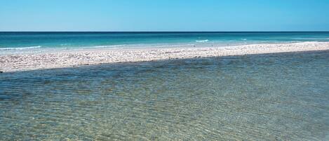 A beach with clear shallow waters leading to a sandy shore.