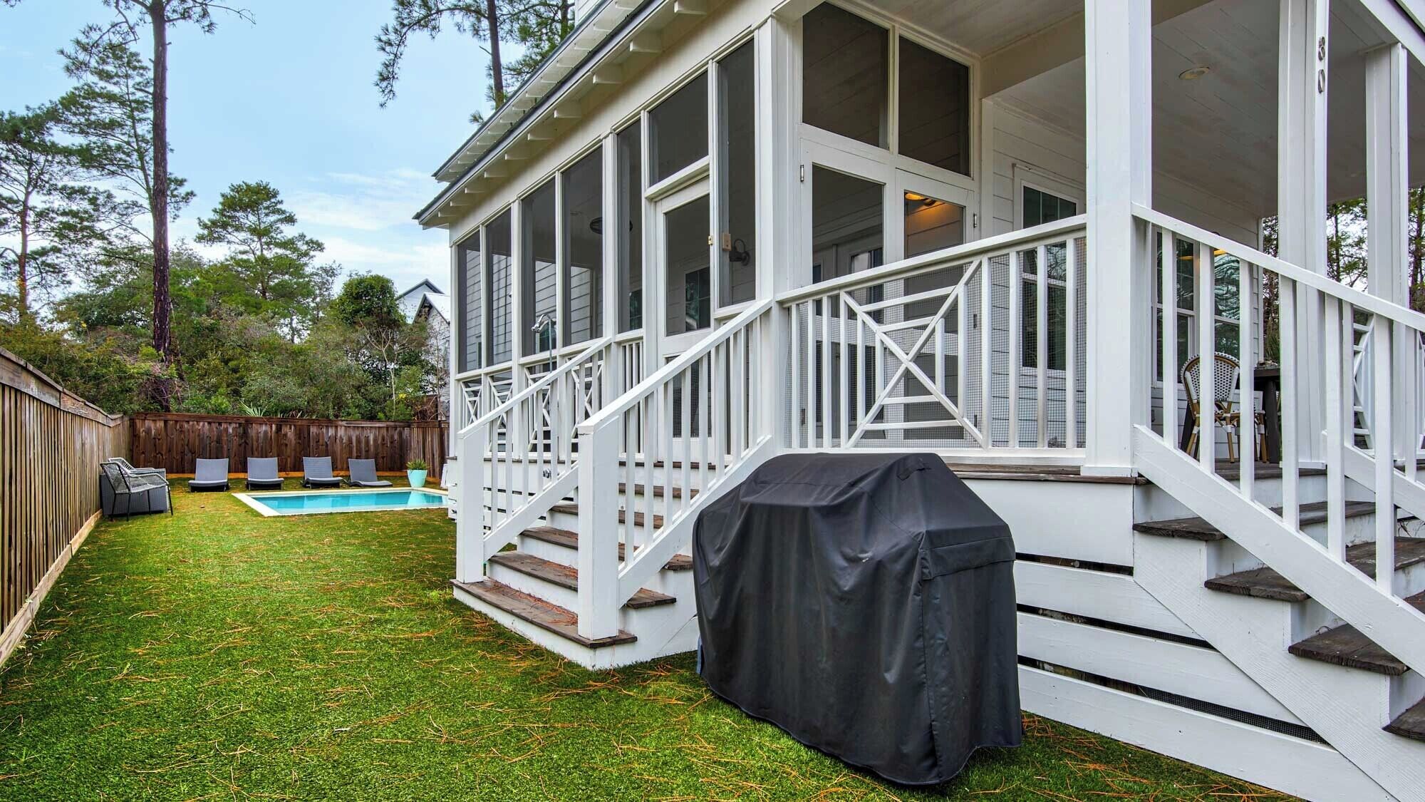 Eine überdachte Terrasse im Freien mit Pool, Grill und einem Holzzaun im Hintergrund.