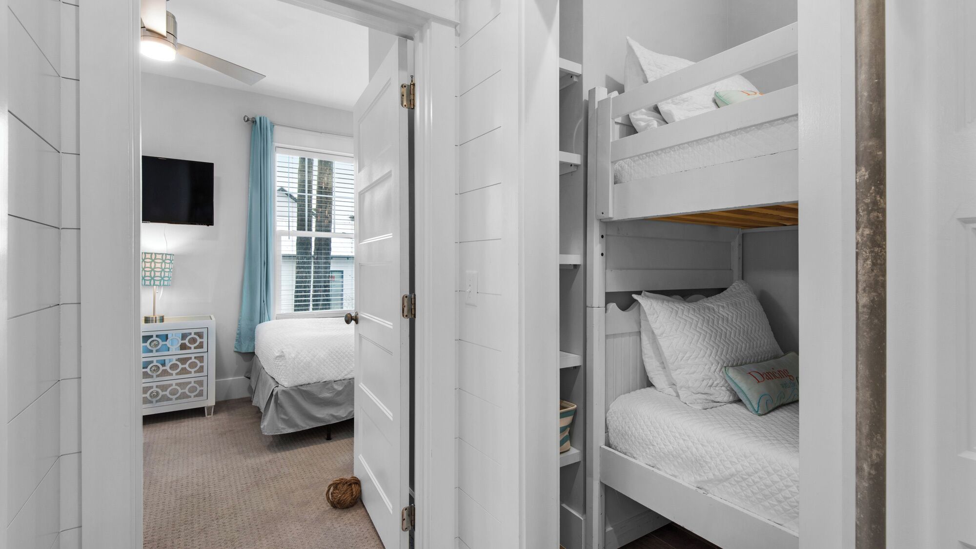 A bedroom with a bunk bed, a bedside table, a lamp, a TV, and a window with curtains.