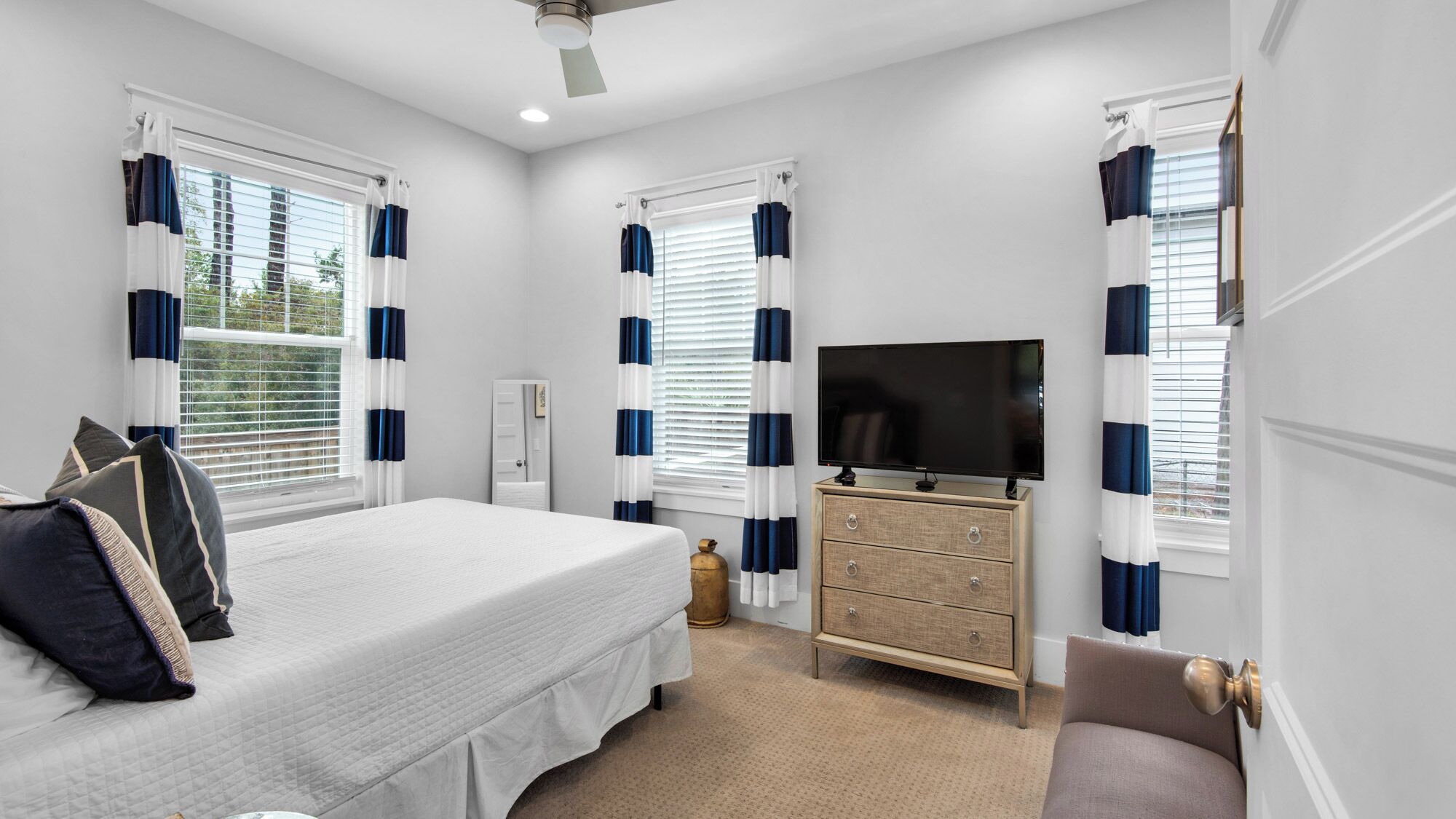 A bedroom with a bed, dresser, TV, and curtains.