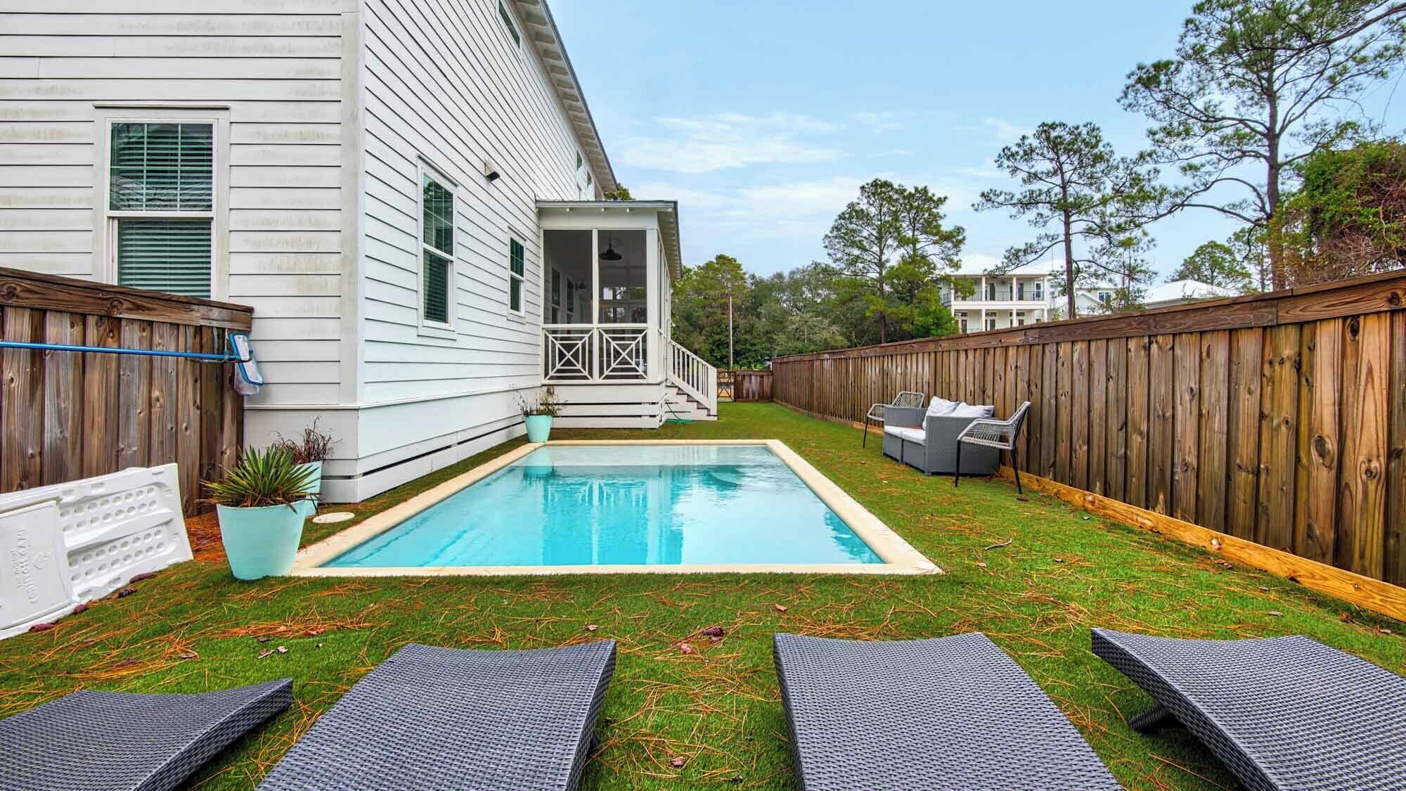 Ein Garten mit Schwimmbad, überdachter Terrasse und Holzzaun.