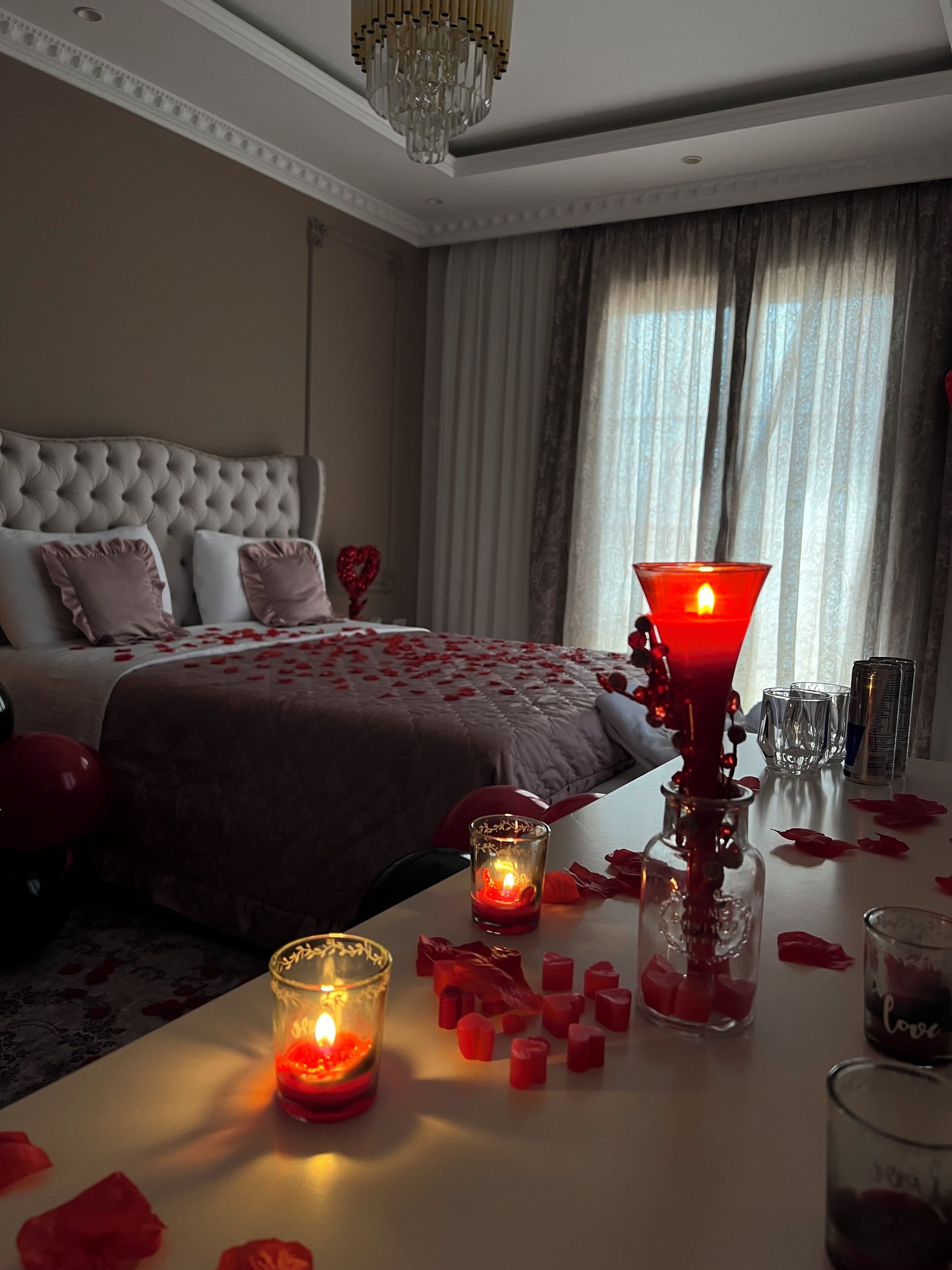 A bedroom with a bed, a chandelier, and candles on the nightstand.