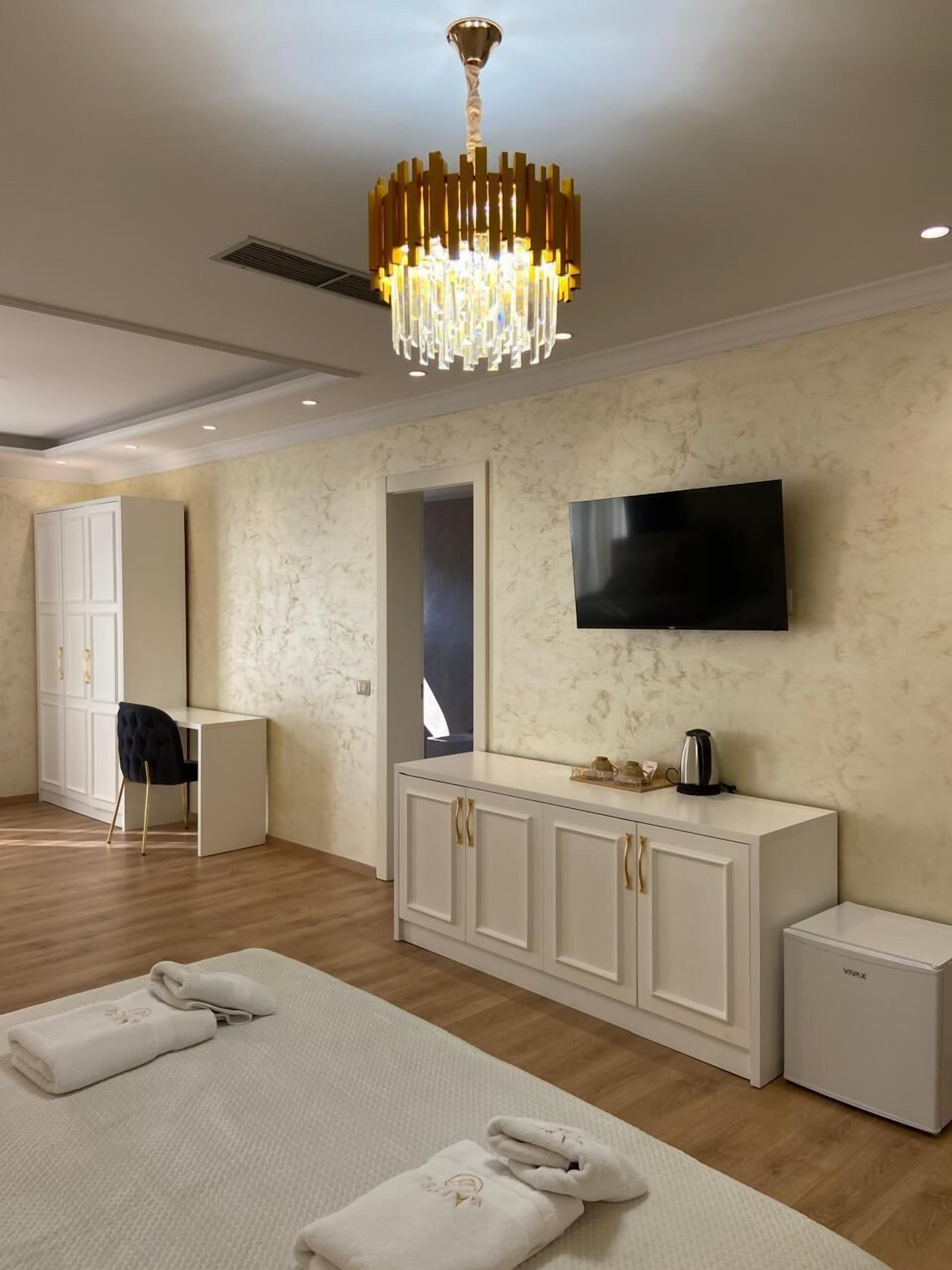 Habitación de hotel moderna con una cama grande, un televisor montado en la pared, una consola blanca y una araña.