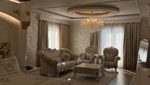 A luxurious bedroom with a large bed, two armchairs, a chaise lounge, a chandelier, and a mirror.
