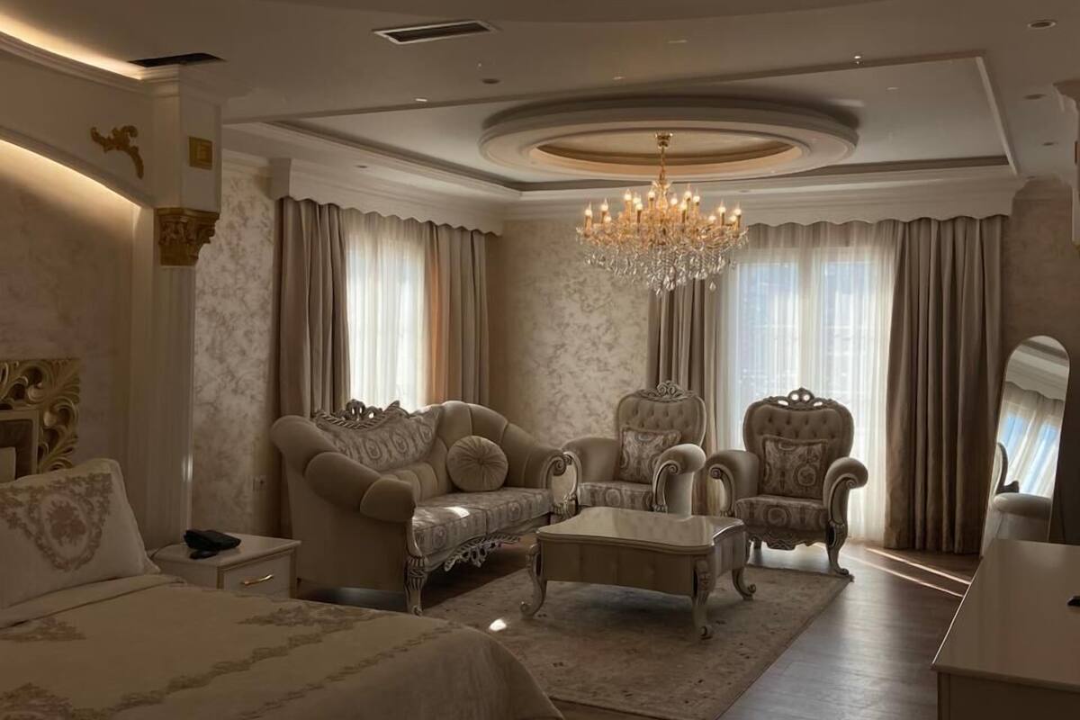 Ein luxuriöses Schlafzimmer mit einem großen Bett, zwei Sesseln, einer Liege, einer Kristallleuchtre und einem Spiegel.
