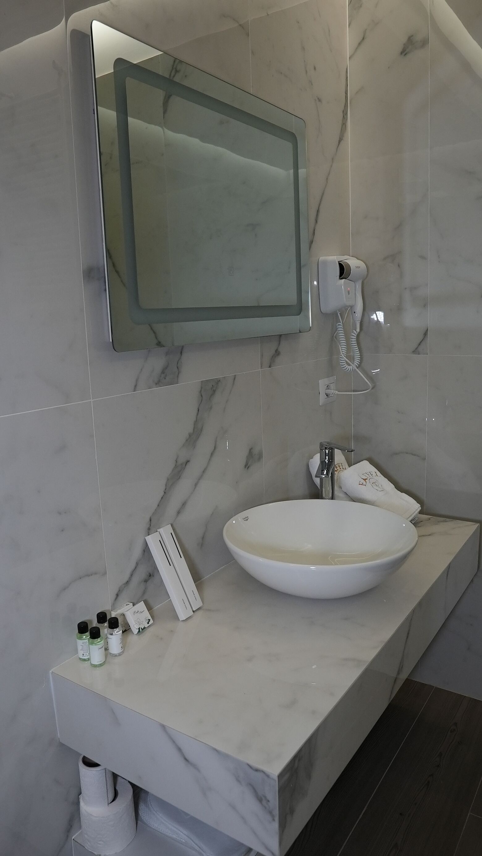 A bathroom with a marble sink, a handheld hair dryer, and toiletries on the counter.