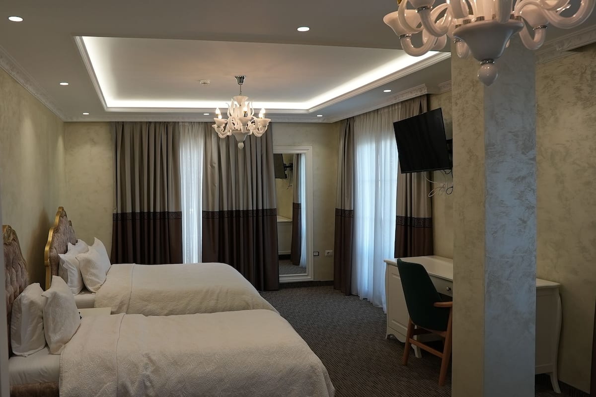 Ein Hotelzimmer mit zwei Betten, einem Schreibtisch, einem Sessel, einem Fernseher und einer Chandelier.