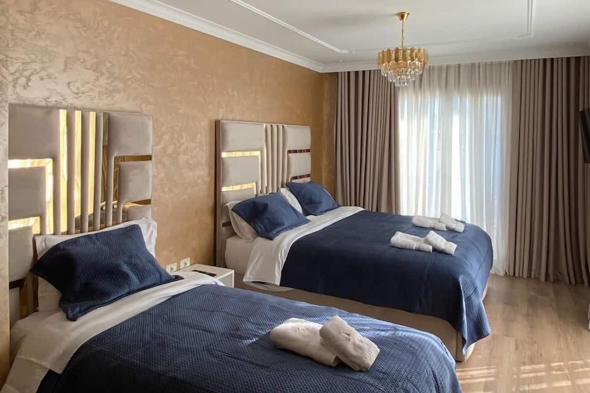 Ein Hotelzimmer mit zwei Betten, einem Chandelier und einem großen Fenster mit Vorhängen.