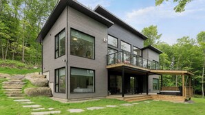 Una casa moderna de dos pisos con ventanas grandes, un balcón y un camino de piedra que conduce a la entrada.
