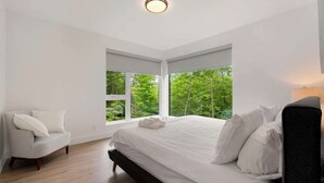 Un dormitorio con una cama grande, dos ventanas, una silla y una mesita de noche.