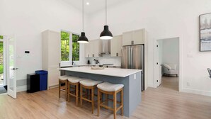 Una cocina moderna con una isla central, taburetes de bar, iluminación colgante y vistas al exterior.