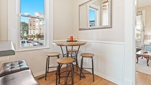 A room with a round table, three stools, a large mirror, and a view of buildings outside. - Indy Stadium Villas 702 (Indianapolis)