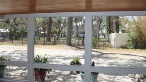 Une vue à travers une fenêtre, avec un plafond en bois, des plantes en pot et un espace extérieur clos, agrémenté d’arbres.