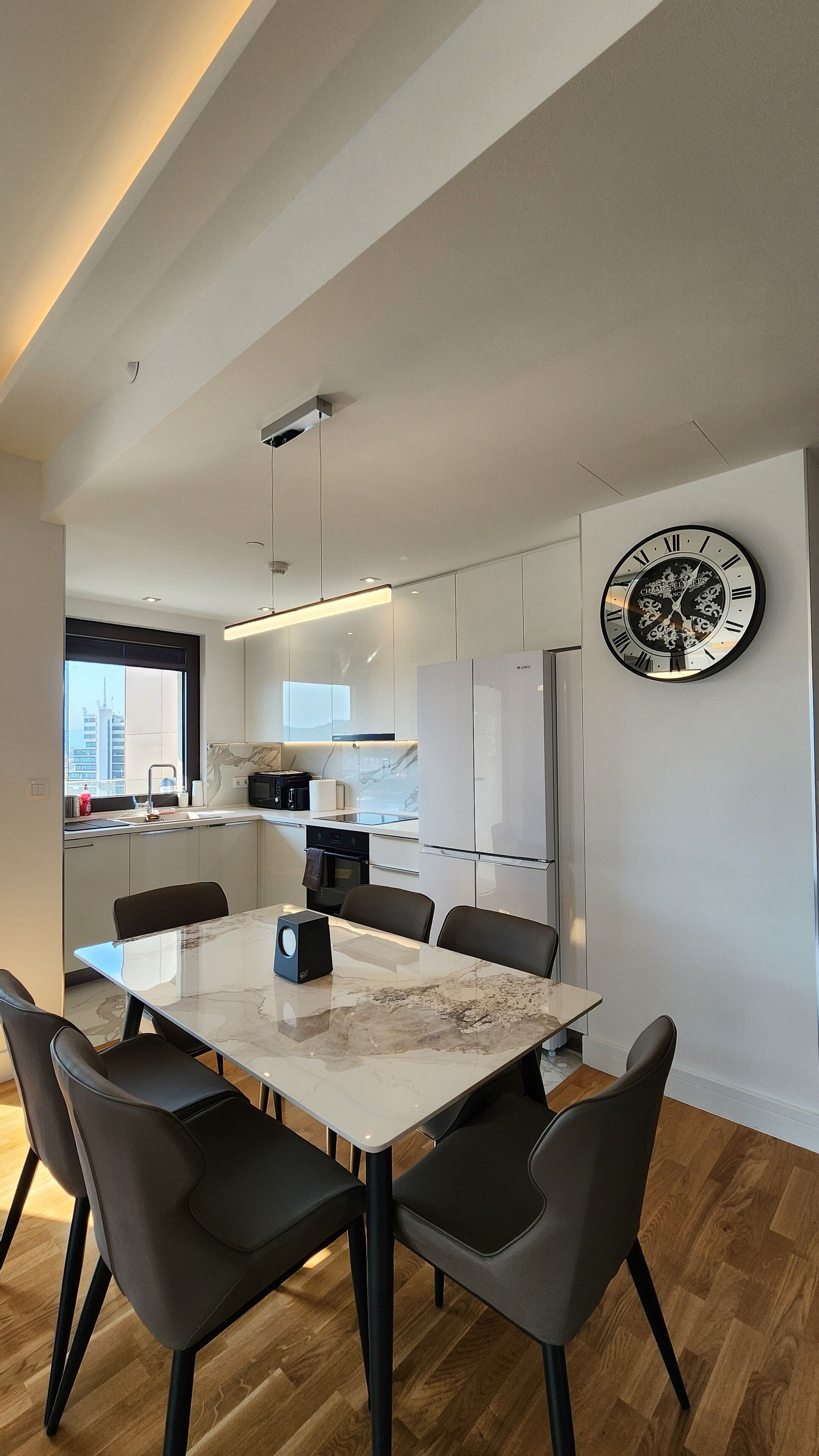 A modern kitchen with white cabinets, a built-in oven, and a large clock on the wall.