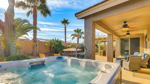 A hot tub with a patio area, palm trees, and a covered seating area with a ceiling fan. - Hot Tub & Heated Pool: Home in Estrella Mtn Ranch (Goodyear)